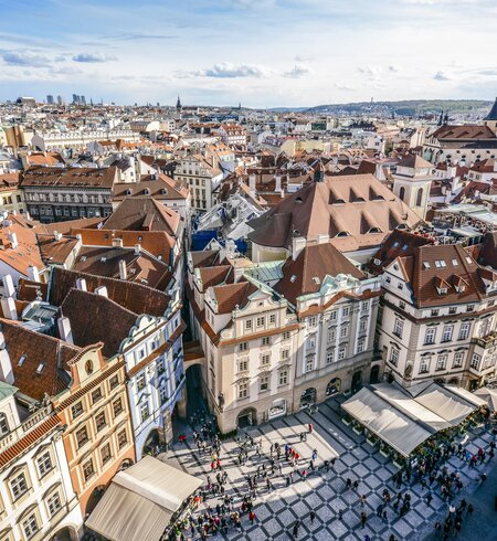 Luftaufnahme über die orangefarbenen Dächer des Altstädter Rings in Prag, Touristen stehen auf dem Platz im Vordergrund. | © Gettyimages.com/AleksandarGeorgiev